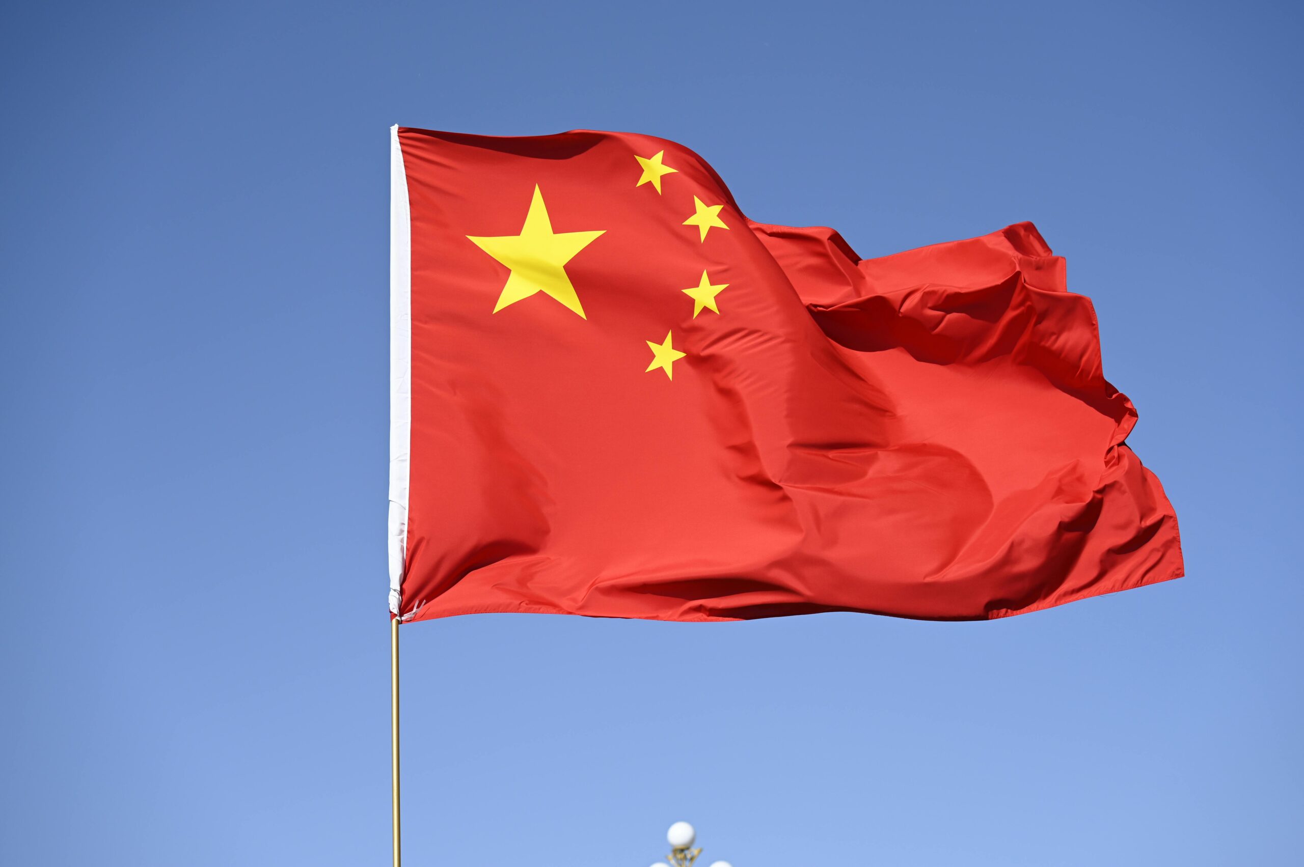 Chinese national flag flying high against a clear blue sky, symbolizing unity and pride.
